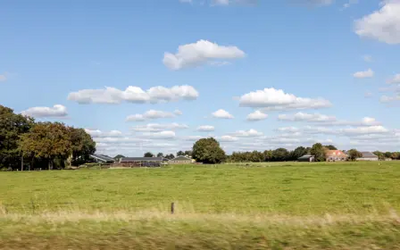 boerderij in landschap met rij bomen en blauwe lucht met witte wolken